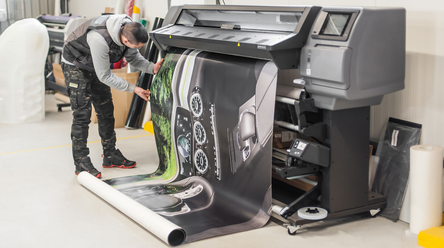 Imprimante UV grand format en cours d'impression d'une bâche PVC haute définition, têtes d'impression appliquant les encres CMYK, opérateur contrôlant les profils colorimétriques sur écran de contrôle